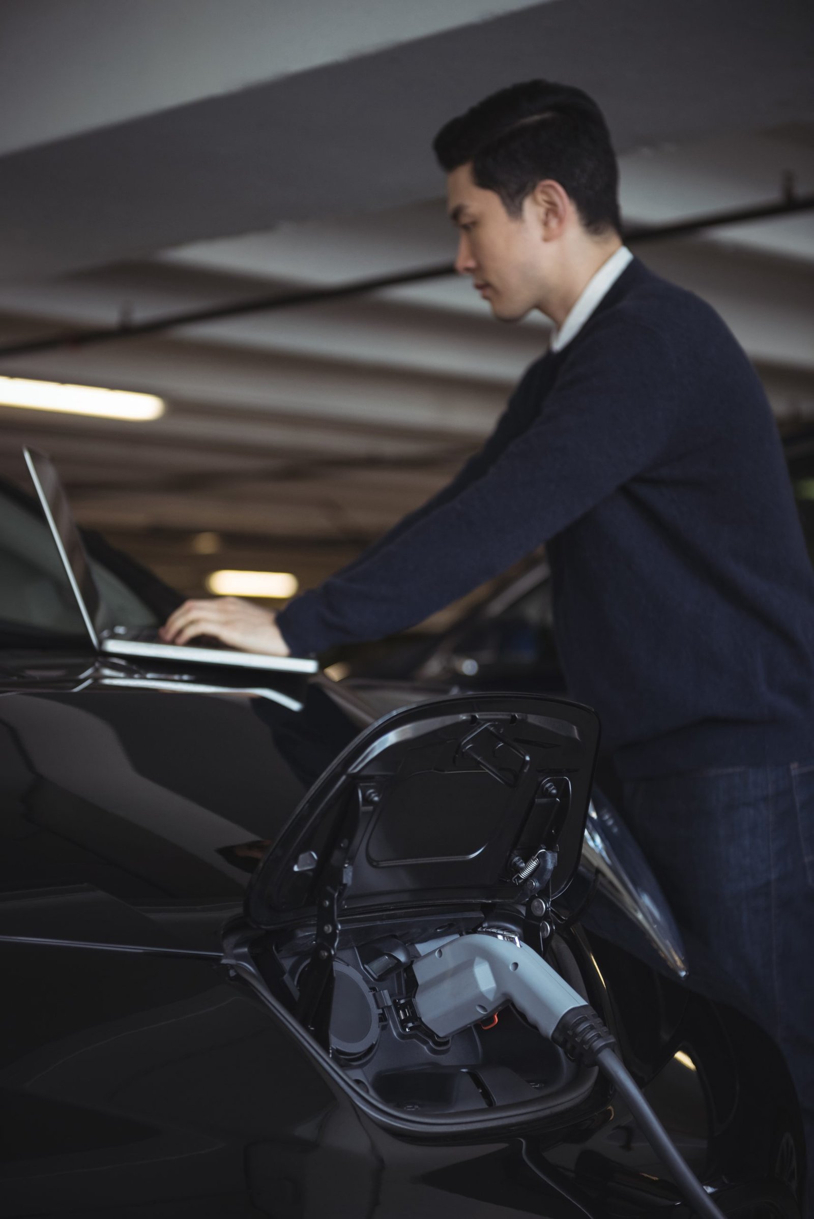 Man using laptop while charging electric car in garage